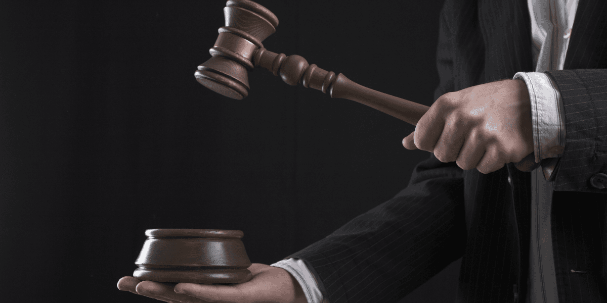A person in a suit holding a gavel above a wooden sound block