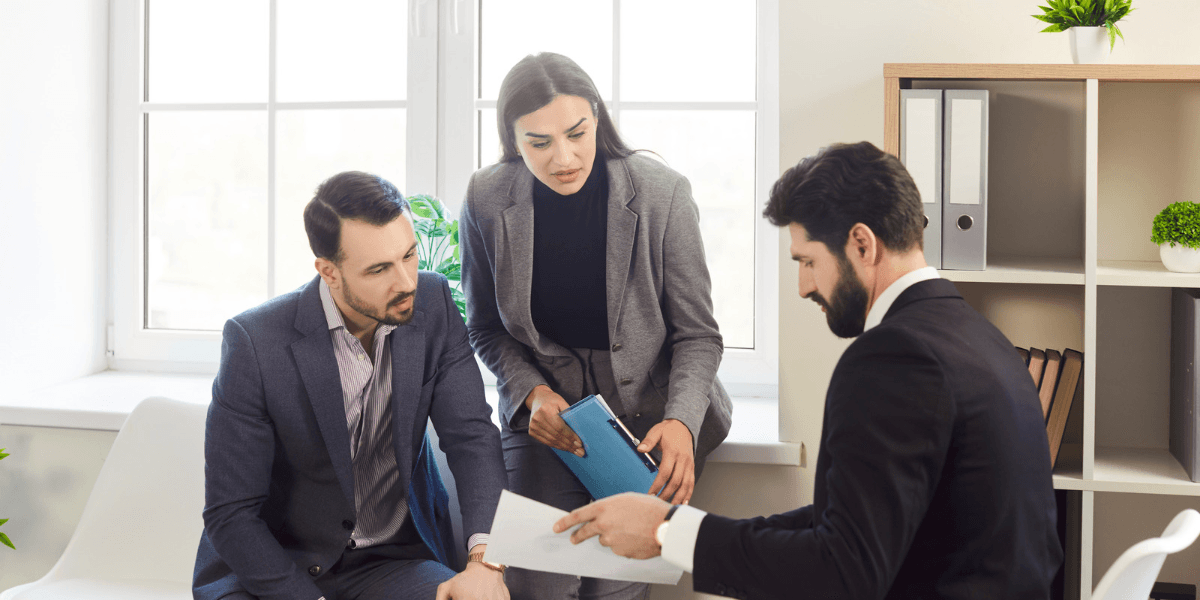 Three professionals in a meeting discussing documents in a bright office setting