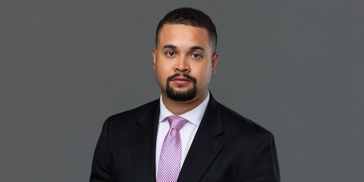 Professional headshot of Associate Attorney Zachary E. Levi wearing a dark suit and pink tie against a gray background.