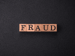 Wooden letter blocks spelling "FRAUD" on a black textured background.