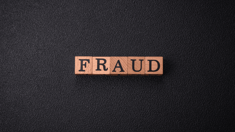Wooden letter blocks spelling "FRAUD" on a black textured background.