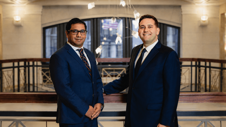Two men in suits smiling indoors with a modern architectural background