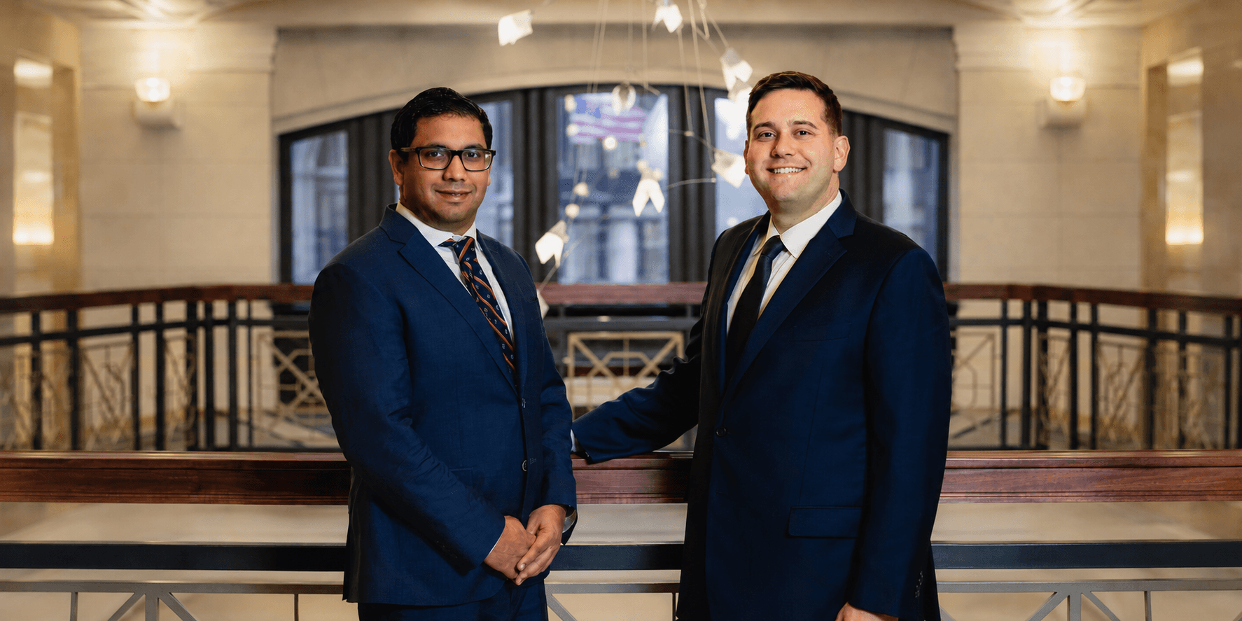 Two men in suits smiling indoors with a modern architectural background