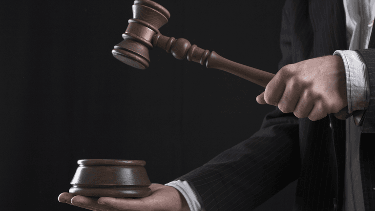 A person in a suit holding a gavel above a wooden sound block