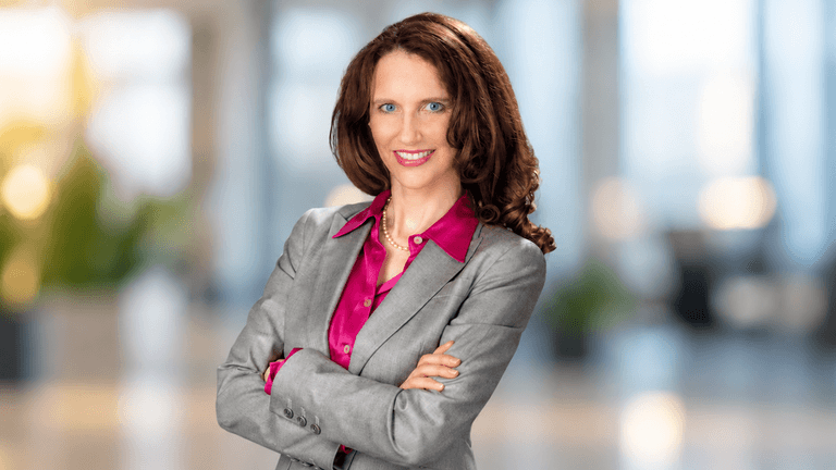 Professional woman in a gray suit and pink blouse standing with arms crossed