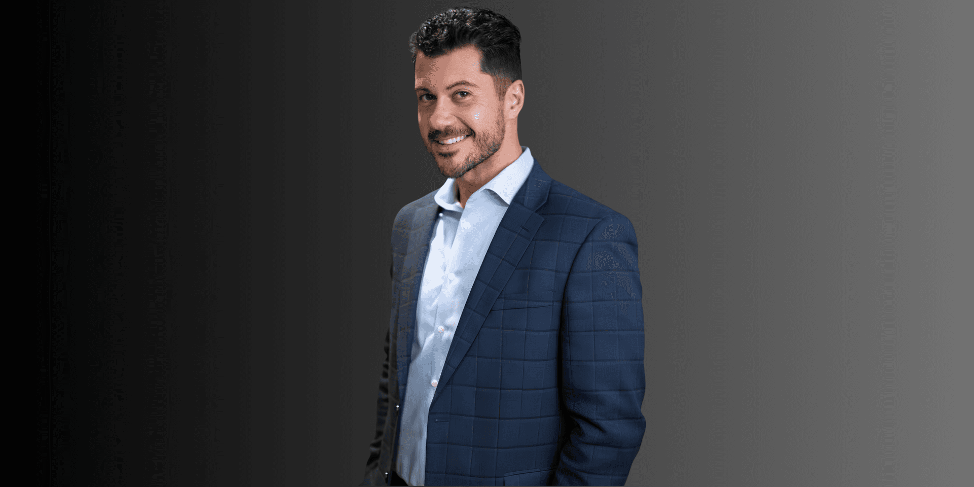 Man in a blue plaid suit smiling against a gradient background