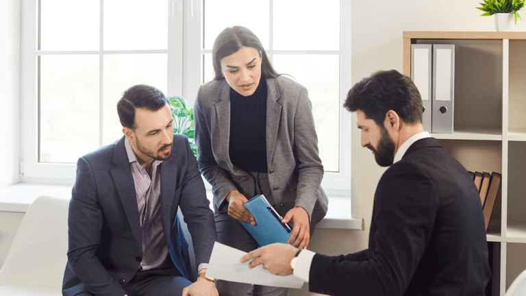 Three professionals in a meeting discussing documents in a bright office setting
