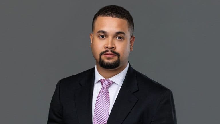 Professional headshot of Associate Attorney Zachary E. Levi wearing a dark suit and pink tie against a gray background.