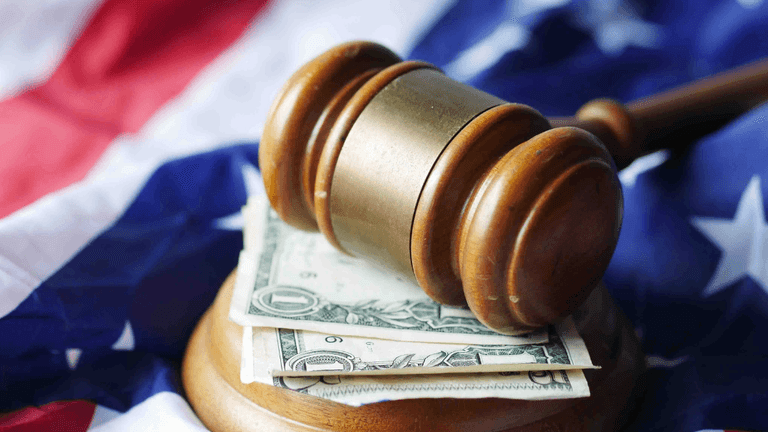 Wooden judge's gavel resting on U.S. currency with an American flag in the background.