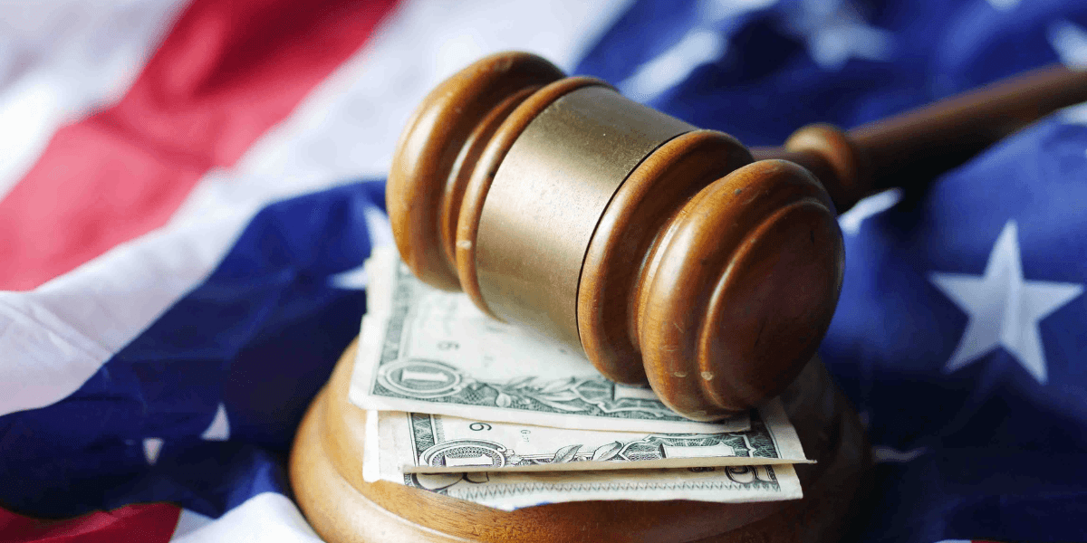 Wooden judge's gavel resting on U.S. currency with an American flag in the background.